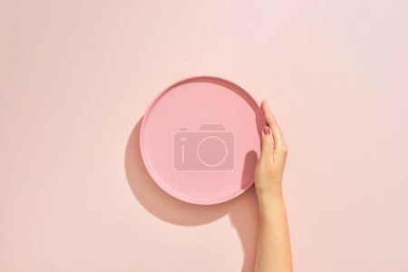 Photo for A female hands hold a empty pink plate on pink table - Royalty Free Image