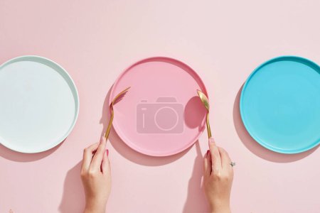 Téléchargez les photos : Restaurant et thème de la nourriture : les mains humaines et vide trois plaques de couleur sur un fond rose - en image libre de droit