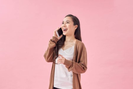 Photo for Positive young asian female smiling and talking smartphone on pink background - Royalty Free Image