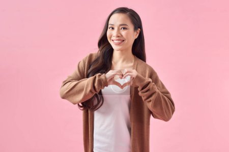 Foto de Retrato aislado de hermosa mujer asiática hacer símbolo del corazón por las manos sobre fondo rosa - Imagen libre de derechos