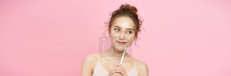 Photo for Woman applying face powder on nose making makeup using cosmetic brush posing over pink - Royalty Free Image