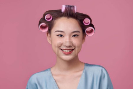 Foto de Hermosa mujer joven en vestido casual y rizadores de pelo sobre fondo rosa - Imagen libre de derechos
