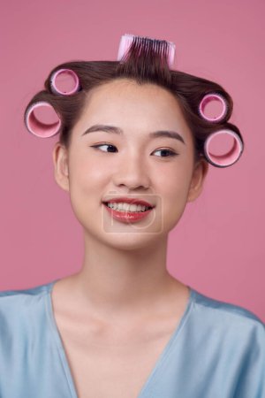 Photo for Happy young woman in blue dress and hair curlers on pink background - Royalty Free Image