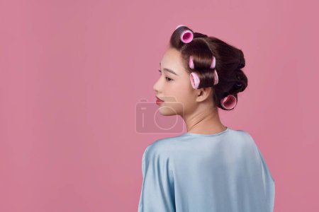 Foto de Seductora joven en rodillos de pelo posando y mirando hacia otro lado sobre fondo blanco - Imagen libre de derechos