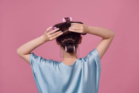 Téléchargez les photos : Vue arrière de la jeune femme avec des bigoudis sur rose - en image libre de droit