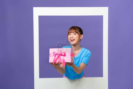 Foto de Foto de divertida mujer joven emocionada sosteniendo caja de regalo dentro de marco de foto blanco sobre fondo de color - Imagen libre de derechos