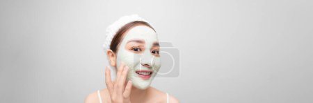 Téléchargez les photos : Soins de la peau. Jeune femme avec masque en argile cosmétique sur bannière blanche - en image libre de droit
