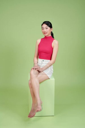 Photo for A seated young smiling woman against green background - Royalty Free Image