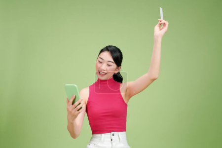 Téléchargez les photos : Jeune femme d'affaires asiatique montrant carte de crédit et téléphone mobile isolé sur vert - en image libre de droit
