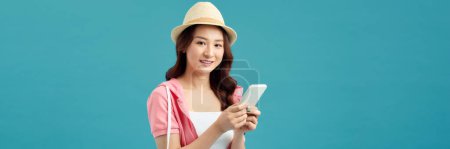 Téléchargez les photos : Portrait de jeune fille asiatique avec téléphone sur fond bleu, concept de vacances d'été - en image libre de droit