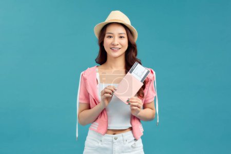 Photo for Happy Asian woman traveler with passport and boarding pass ticket isolated on blue background - Royalty Free Image