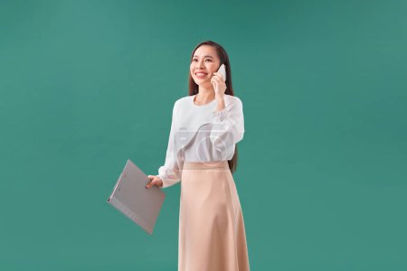 Téléchargez les photos : Businesslike femme heureuse tenant presse-papiers avec des fichiers dans le bureau et appelant avec téléphone mobile - en image libre de droit