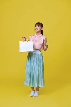 Téléchargez les photos : Jeune femme d'affaires asiatique tenant des sacs à provisions posant sur fond jaune - en image libre de droit