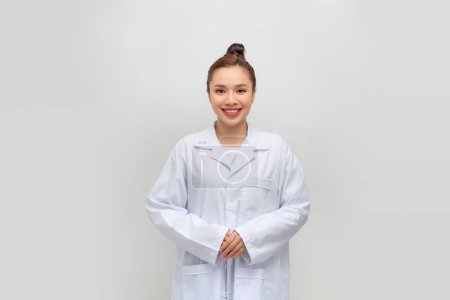 Foto de Feliz joven doctora en uniforme médico sonriendo mientras está de pie con los brazos cruzados - Imagen libre de derechos