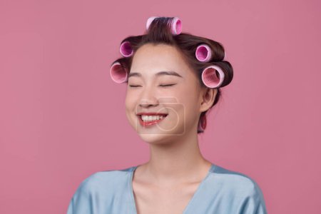 Foto de Muchacha sonriente atractiva con rizadores de pelo en la cabeza rizando el cabello para rizos perfectos - Imagen libre de derechos