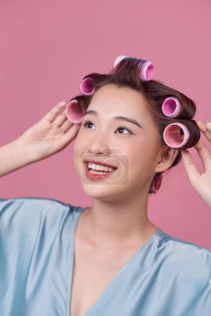 Foto de Mujer joven pensativa en rulos de pelo posando sobre fondo rosa - Imagen libre de derechos
