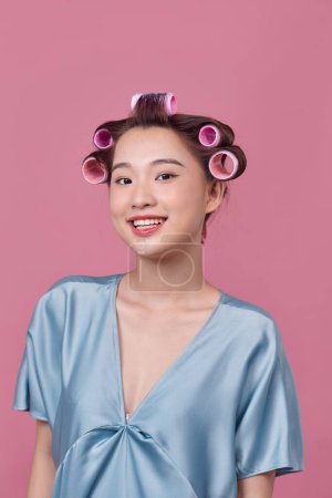 Foto de Alegre joven modelo posando con rizadores de pelo sobre fondo rosa - Imagen libre de derechos