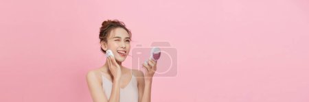 Téléchargez les photos : Young attractive lady applying cushion on her face with powder puff on pink background - en image libre de droit