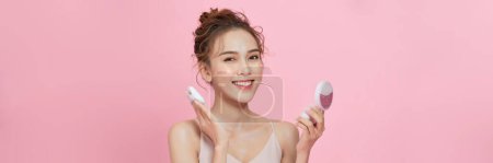 Photo for Young attractive lady applying cushion on her face with powder puff on pink background - Royalty Free Image