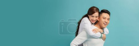 Téléchargez les photos : Happy smiling young asian couple piggyback isolated on light blue background - en image libre de droit
