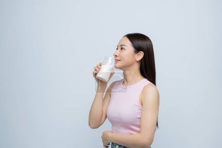 Foto de Una joven asiática satisfecha bebiendo leche del vaso aislado sobre fondo blanco - Imagen libre de derechos