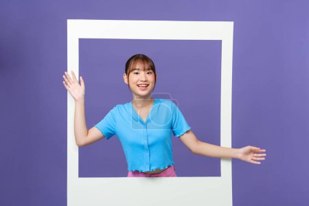Foto de Photo of shiny funny young lady smiling looking through white window isolated on purple background - Imagen libre de derechos