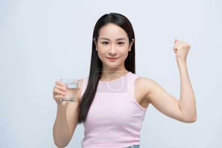 Foto de Sonriente joven asiática sosteniendo un vaso de agua limpia fresca con el brazo levantado en blanco - Imagen libre de derechos