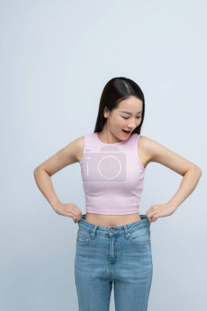 Photo for Young smiling happy woman show loose pants on waist after weightless isolated on white background. - Royalty Free Image