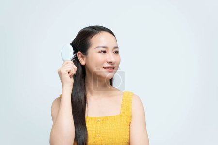 Téléchargez les photos : Heureuse jeune femme peigner ses longs cheveux sains sur fond blanc
. - en image libre de droit