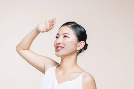 Beautiful young Asian woman raise arm to cover the sun with clean fresh skin on beige background.
