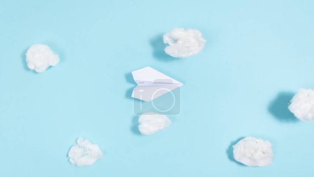 Foto de White paper airplane flies through white clouds on a blue background. Concept of travel, trips, air delivery. Flat lay. Copy space. - Imagen libre de derechos