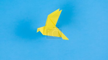 Foto de Yellow paper origami dove flies. Blue background. Symbol of peace. Concept of help, support and peace for Ukraine in fight against Russian aggression. - Imagen libre de derechos