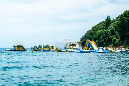 Foto de Playa de Morgen, Montenegro - 4 de julio de 2021: Personas en atracciones acuáticas de entretenimiento inflables y toboganes en el mar. Budva Rivera.. - Imagen libre de derechos