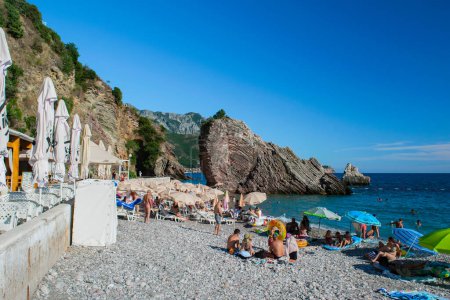 Photo for Rafailovici, Montenegro - July 01, 2021: Resting people on pebble public stone beach with beautiful puff rocks. Adriatic Sea. Summer sunny day. Seaside vacation resort season. - Royalty Free Image