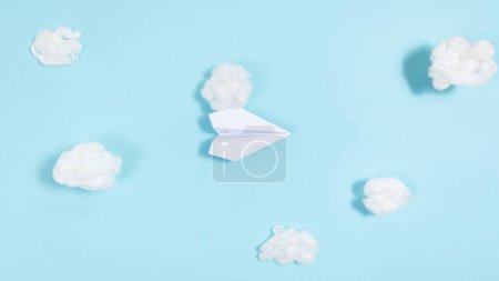 L'avion en papier blanc vole à travers des nuages blancs sur un fond bleu. Concept de voyage, voyages, transport aérien. Pose plate. Espace de copie.