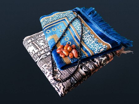 Folded Muslim prayer mat used to pay with tasbeeh and khajoor (Dates) on dark background