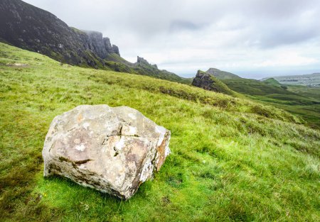 Photo for Quiraing,Isle of Skye,Scotland,UK-July 25 2022: Hikers walk along the mountain paths of the Quraing mountain range,a large boulder in the foreground,on a summer afternoon. - Royalty Free Image
