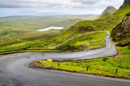 Téléchargez les photos : Route de montagne pour la circulation visitant le sentier pédestre de Quiraing, parmi de beaux paysages spectaculaires, descendant vers la côte, par un jour pluvieux de milieu d'été.Nord-Est de Skye. - en image libre de droit