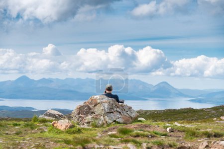 Foto de Applecross peninsula, Highlands of Scotland, UK-July 28 2022: Un viajero y excursionista, disfruta de las vistas a mediados del verano, desde la cima del paso de alta montaña, con vistas al hermoso paisaje escocés. - Imagen libre de derechos