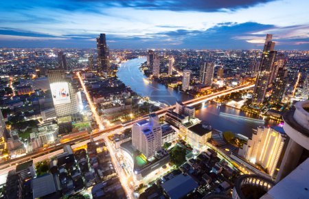 Téléchargez les photos : Bangkok,Thailand-December 04 2022: Viewed from a skyscraper rooftop, thousands of lights illuminate Thailand's capital city,and light trails from traffic and boats moving along Chao Pharya river. - en image libre de droit
