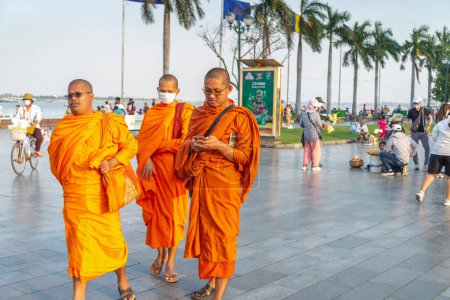 Photo for Phnom Penh,Cambodia-December 23rd 2022:Dressed in traditional orange robes,Khmer monks casually walk along Sisowath Quay at sunset,enjoying the relative cool of early evening. - Royalty Free Image