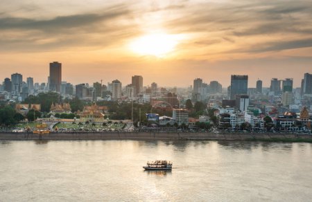 Photo for Rooftop view,looking across to the Riverside area of Cambodia's capital city.Sunset over Royal Palace and high rise buildings as a small boat drifts by towards the Mekong river intersection. - Royalty Free Image