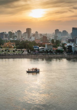 Photo for Rooftop view,looking across to the Riverside area of Cambodia's capital city.Sunset over Royal Palace and high rise buildings as a small boat drifts by towards the Mekong river intersection. - Royalty Free Image