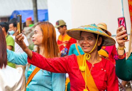 Photo for Pai,Northern Thailand-April 4th 2023:Women take pictures of the passing street procession,attended by hundreds of Thais,where boys are ordained to be Buddhist monks. - Royalty Free Image
