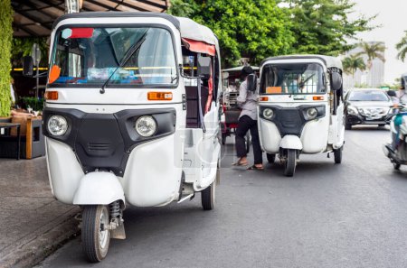 Foto de Vehículos blancos brillantes de tres ruedas, con asiento trasero y un conductor, con techo cubierto, esperando junto a la carretera en la ciudad capital de Camboya, una forma popular y barata de transporte. - Imagen libre de derechos
