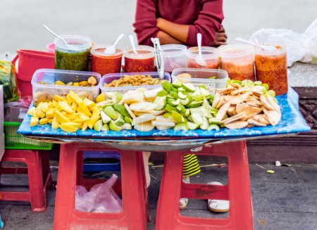 Photo for Tasty morsels including mango,papaya,dates and a variety of spicy sauces,on display,for passing pedestrians,on a small colorful stall on the river wall at sunset. - Royalty Free Image