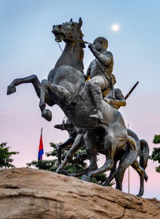 Photo for Placed on a large rock,moonshine at dusk,along Riverside walk.Life-size bronze sculpture of two horses,one rearing up defiantly,mounted by heroic,historic soldiers,against pink afterglow of sunset. - Royalty Free Image