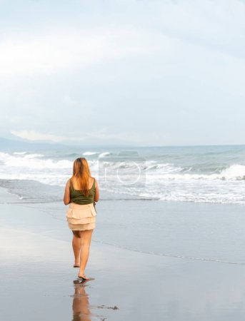 Foto de Sosteniendo su teléfono para selfies, en una playa cerca de Manila al atardecer, paseando sin rumbo por las cálidas aguas costeras, a lo largo de arenas suaves, divirtiéndose, bailando, pateando las suaves olas mientras entran. - Imagen libre de derechos