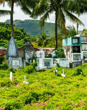 Foto de Interesante cementerio, junto al mar en Oslob, lleno de muchas tumbas, tumbas y cámaras que albergan a los fallecidos, cientos de crucifijos blancos, situado entre, selva tropical, palmeras junto a la pared del mar y la playa. - Imagen libre de derechos
