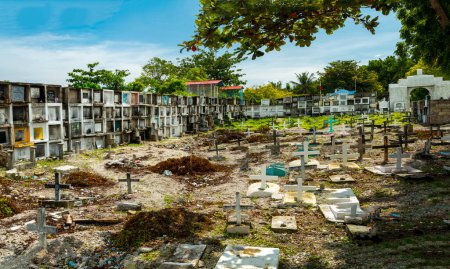Foto de Atmosférico cementerio católico filipino, junto al mar del estrecho de Cebú, muchas tumbas con cámara, que alberga a los fallecidos, cientos de crucifijos, marcando tumbas, dispuestos al azar, por el muro del mar y la playa. - Imagen libre de derechos